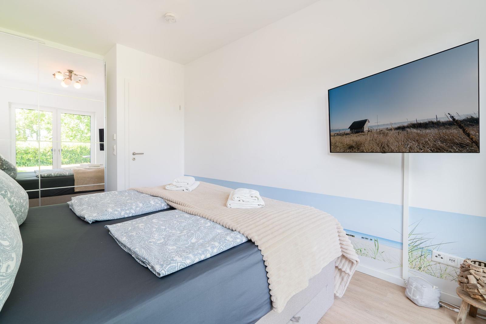 Bedroom with bed, TV, and window. Wall with beach motif.