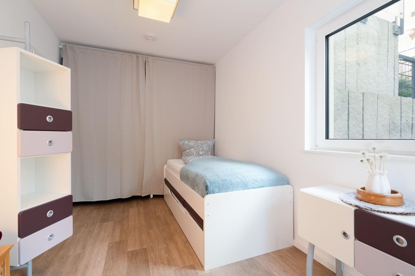 A bedroom with single bed, wardrobe, and nightstand. Window and wooden floor.