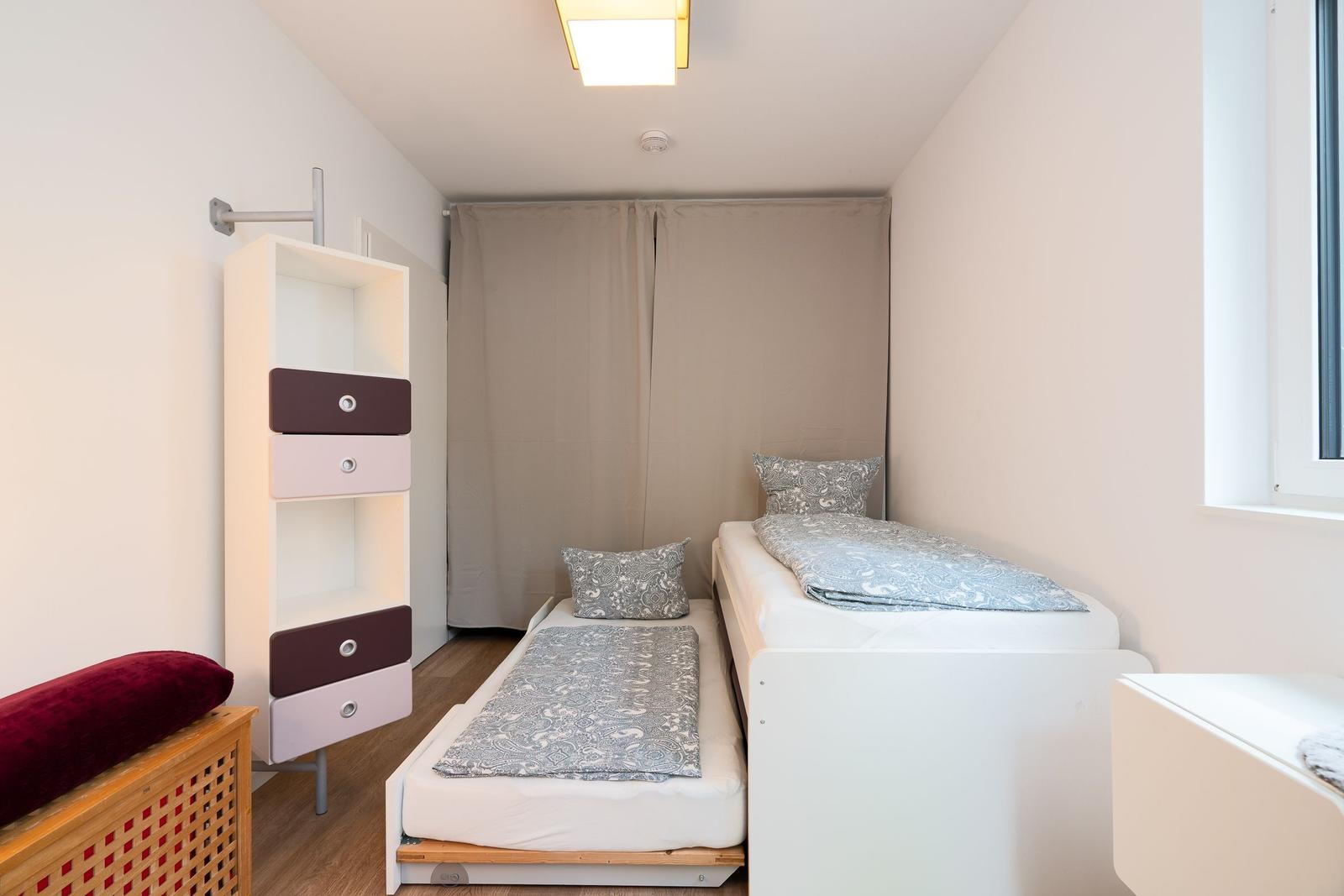 Room with two beds, wardrobe, and window. Bedding in gray.