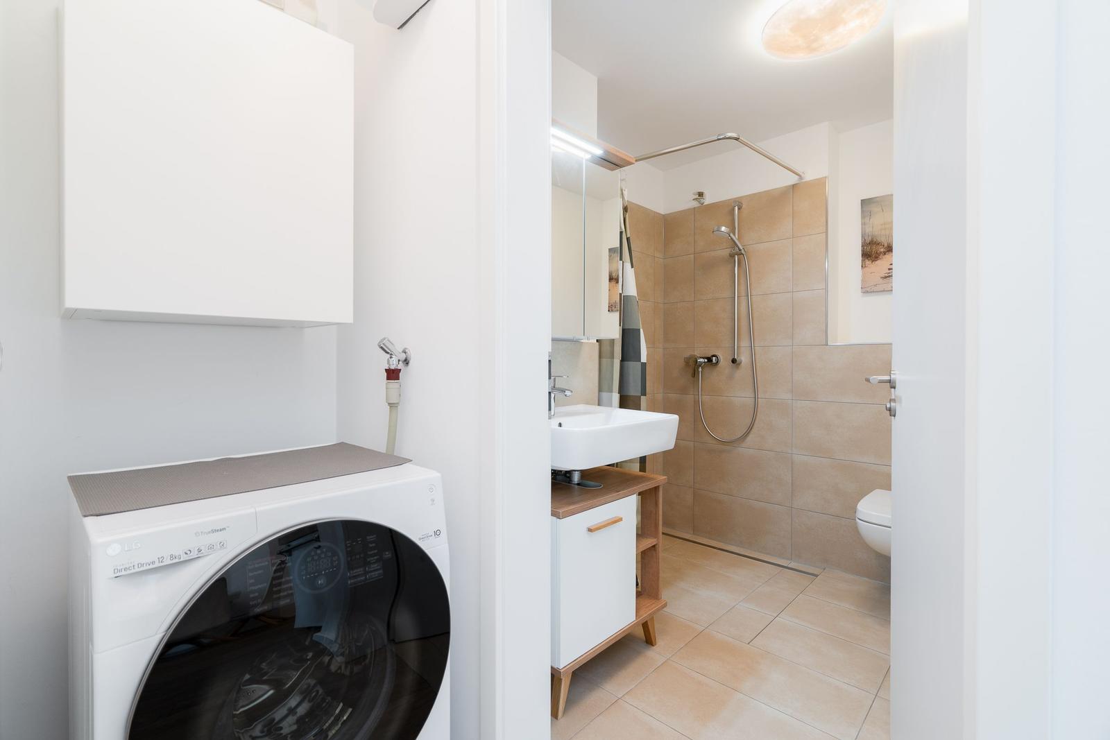 Washing machine next to bathroom with shower and sink