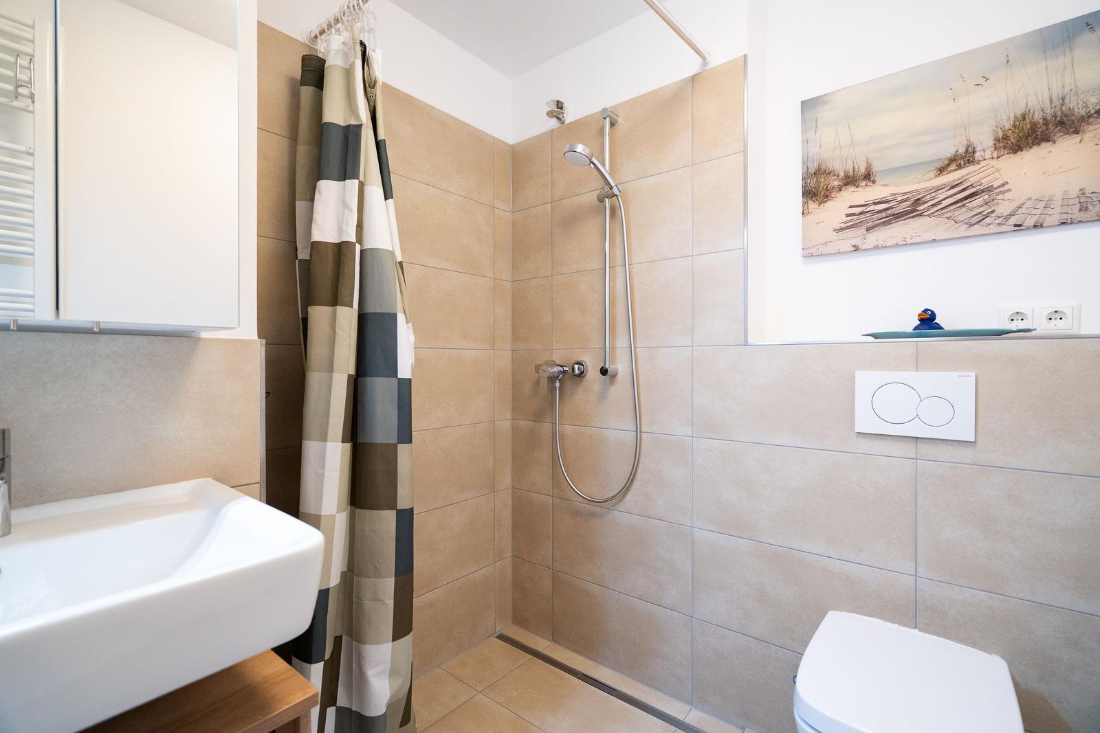 Bathroom with shower, sink, and toilet. Wall picture and shower curtain visible.
