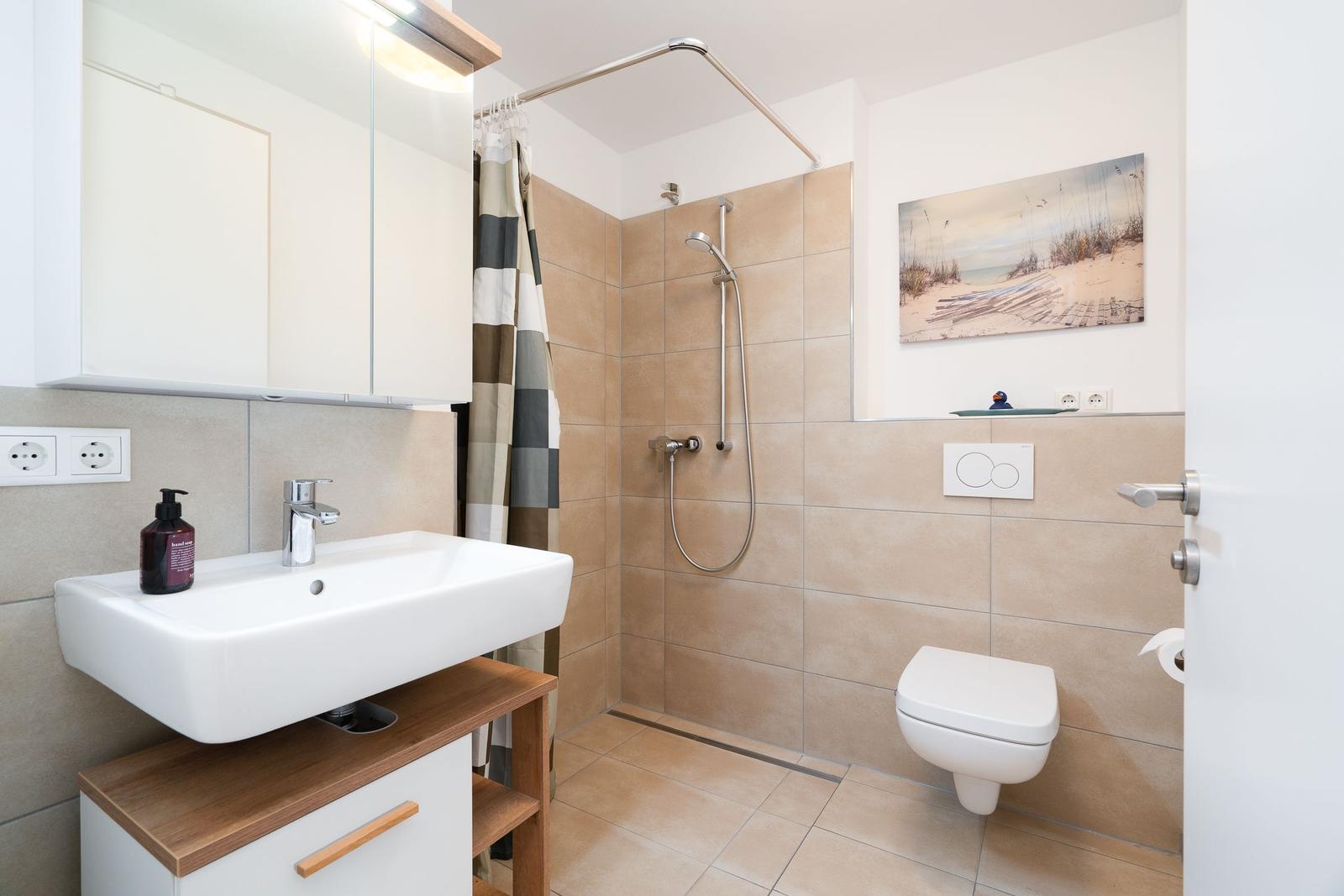 Bathroom with shower, sink, and toilet. Wall art and shower curtain are visible.