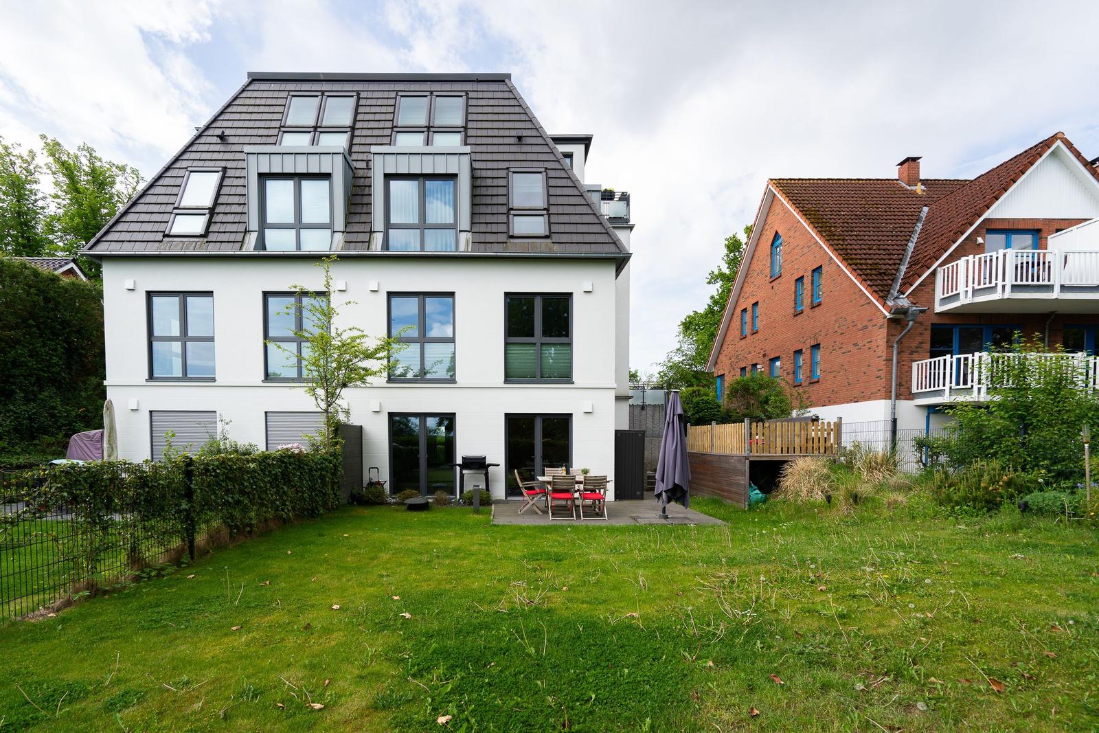 Modern villa with garden, terrace, and grill area. Next to a red brick house.