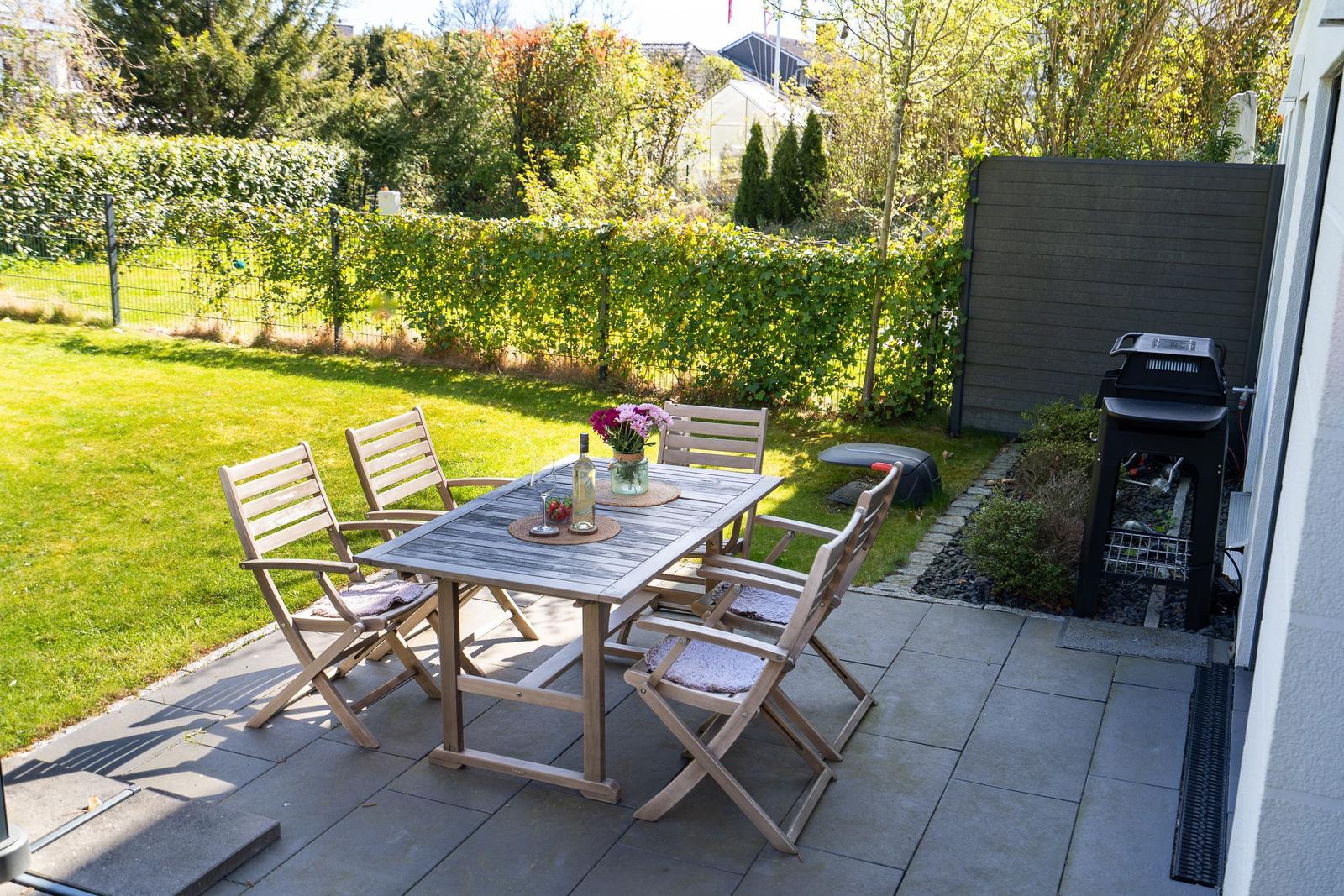 Terrace with table, four chairs, grill, and green lawn.