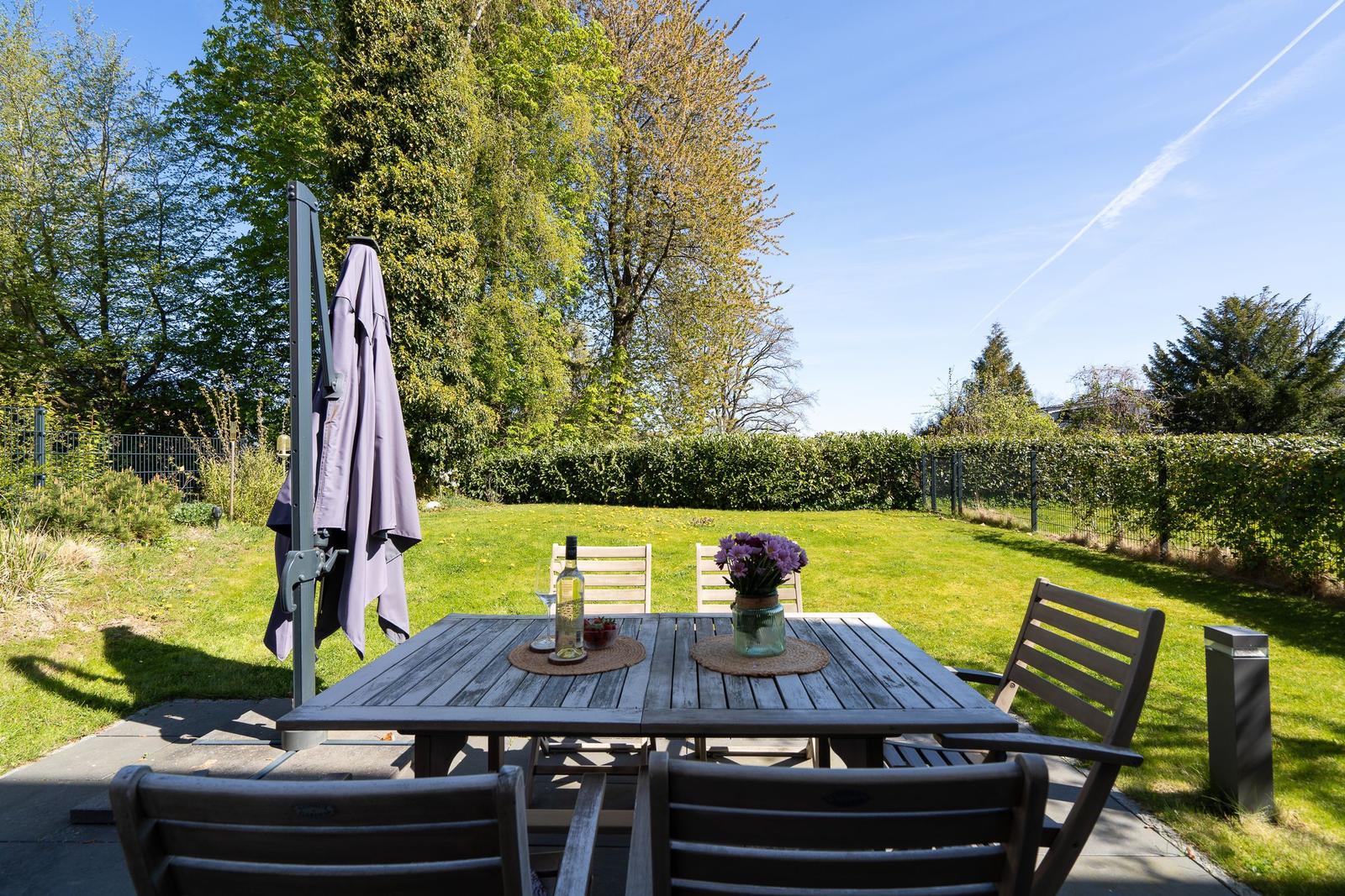 Wooden table with chairs and umbrella in the garden. Lawn and hedge in the background.