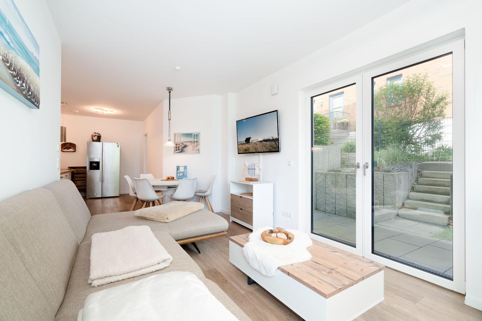 Living room with sofa, coffee table, and TV. Access to kitchen and terrace.