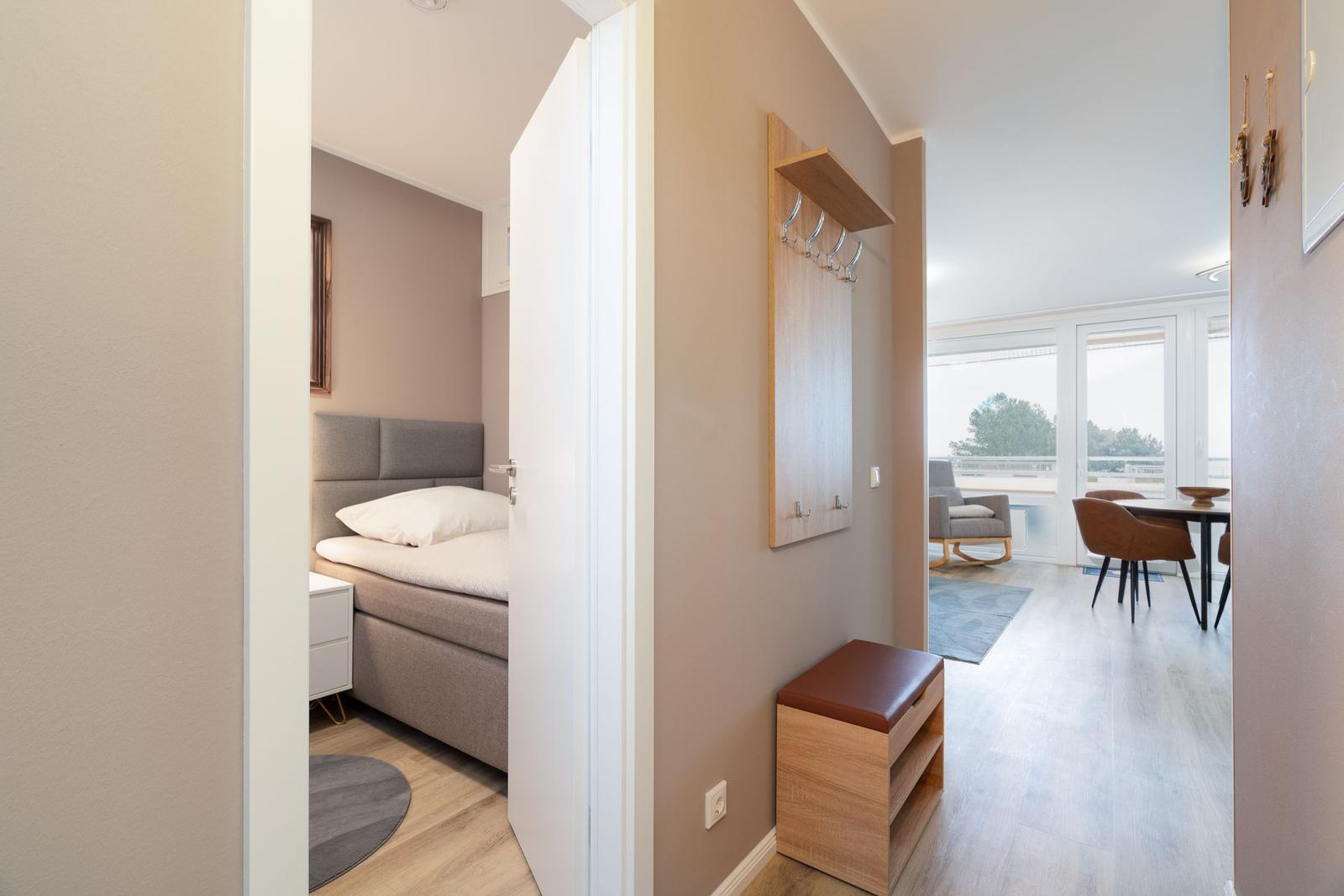 Bedroom with bed and nightstand. Hallway to living and dining area with table, chairs, and balcony.