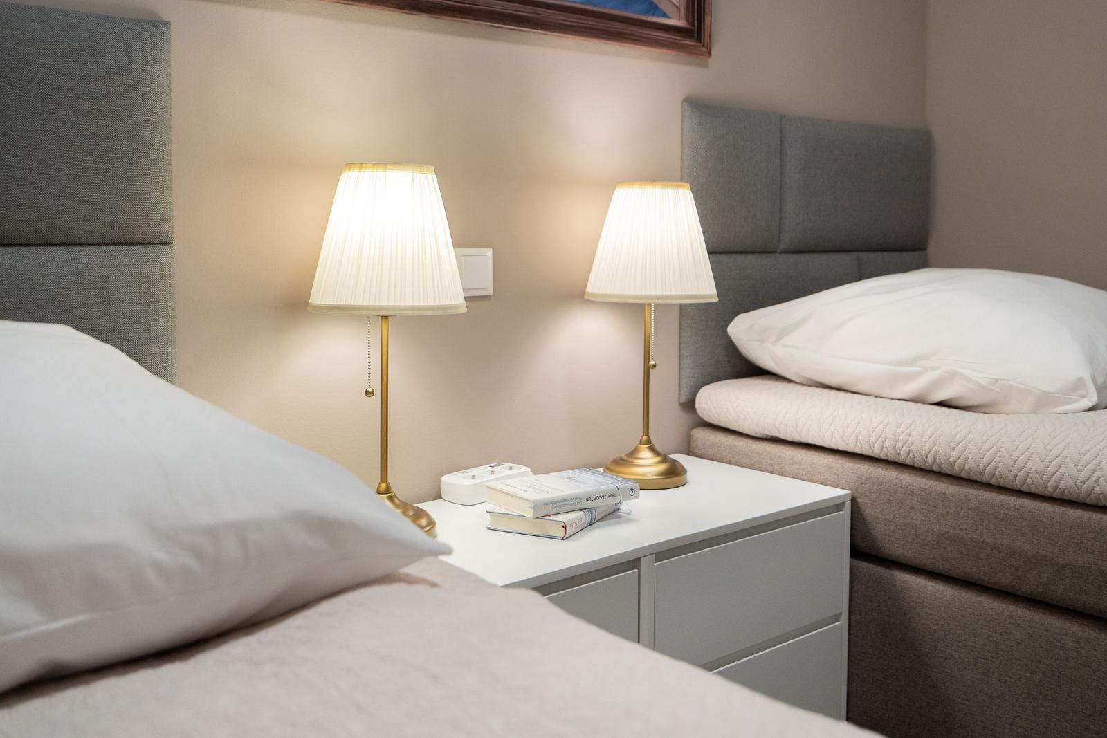 Two beds with headboards and nightstand with lamps and books.