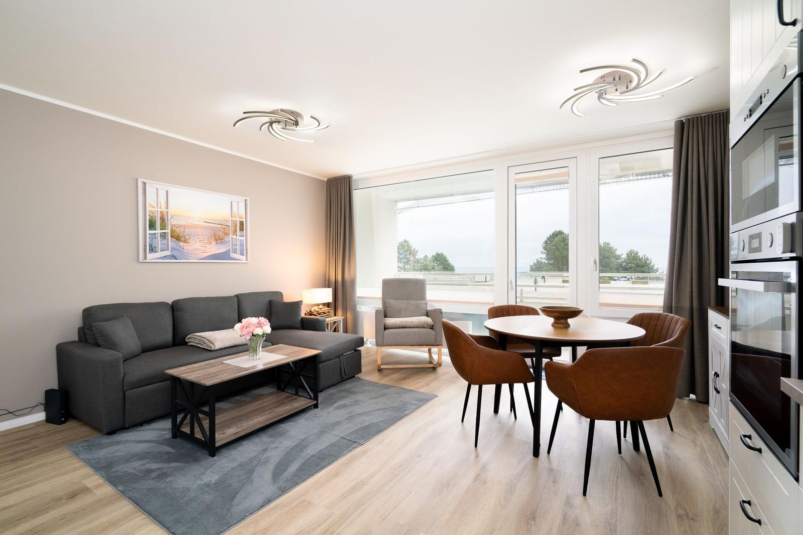 Living and dining area with sofa, table and chairs. Large windows with view of the outdoor area.