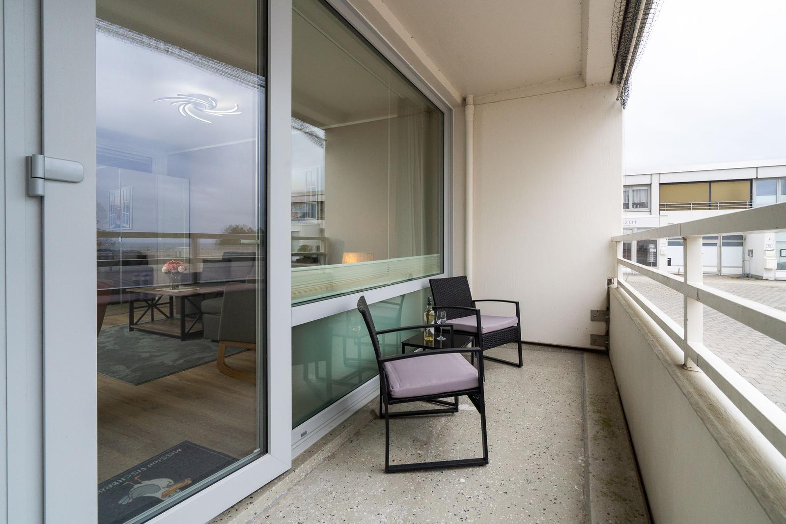 Balcony with two chairs and a small table. Glass doors lead into the apartment.