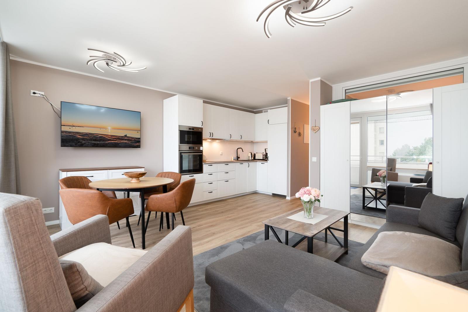 Apartment with kitchen, dining area, and living room. TV, table, sofa, and flowers.