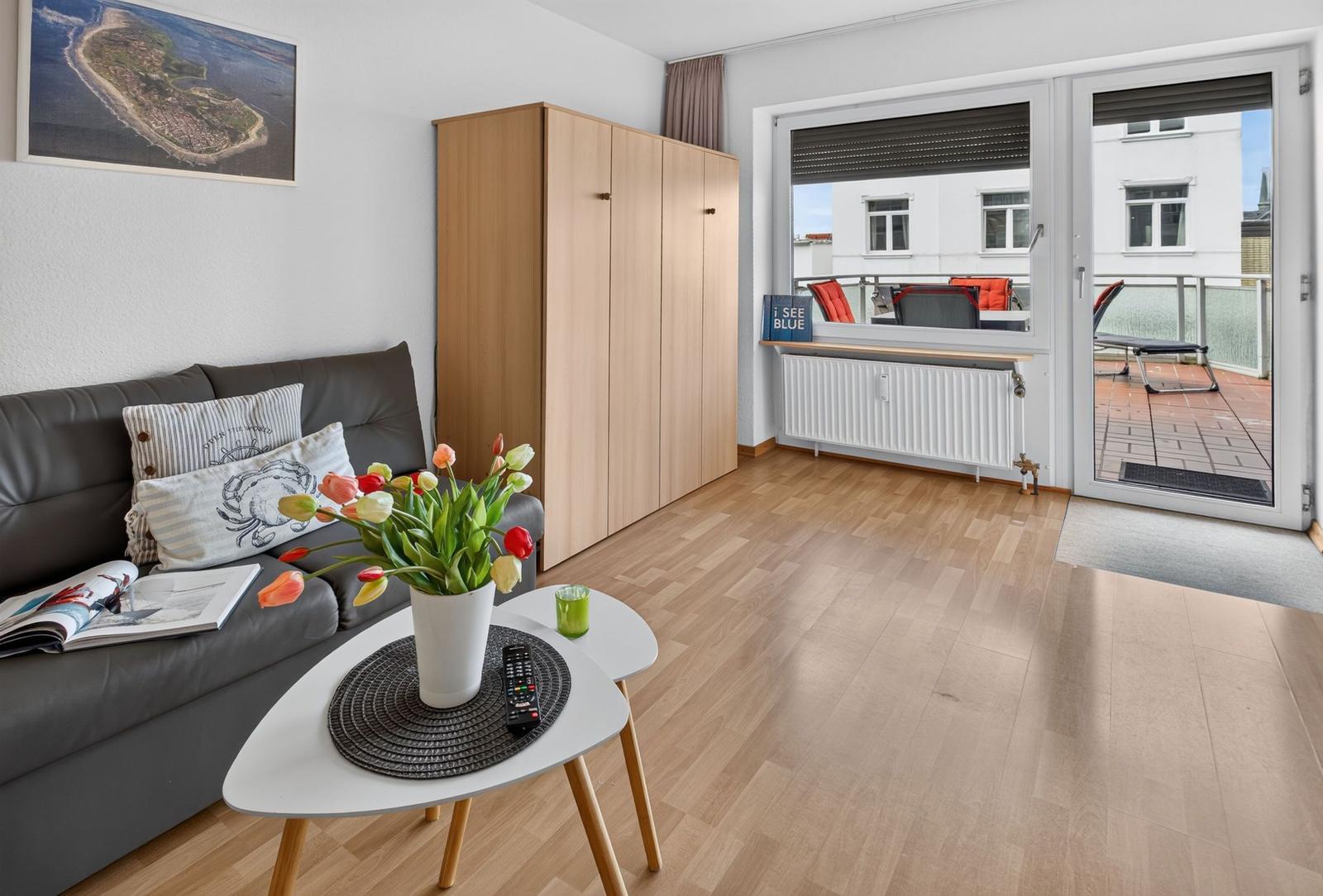Wohnzimmer mit Sofa, Tisch und Balkon. Holzfußboden und Kleiderschrank.