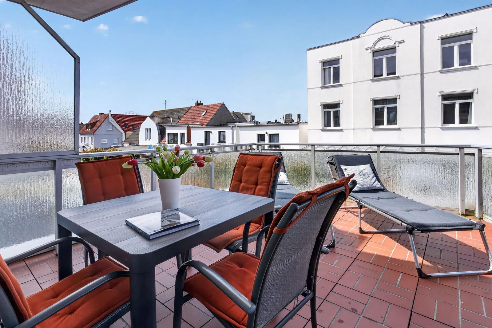 Terrasse mit Tisch, Stühlen und Liege. Blick auf Gebäude und Himmel.
