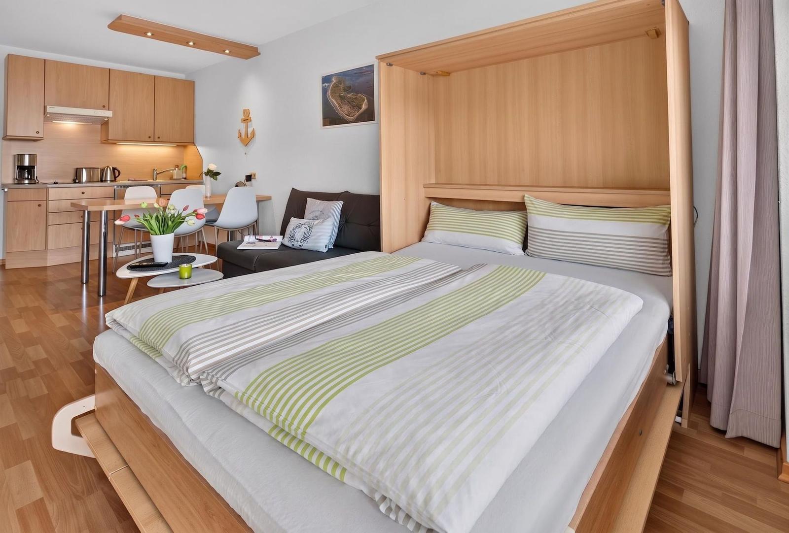 Ein Schlafzimmer mit Bett und Küchenbereich im Hintergrund.