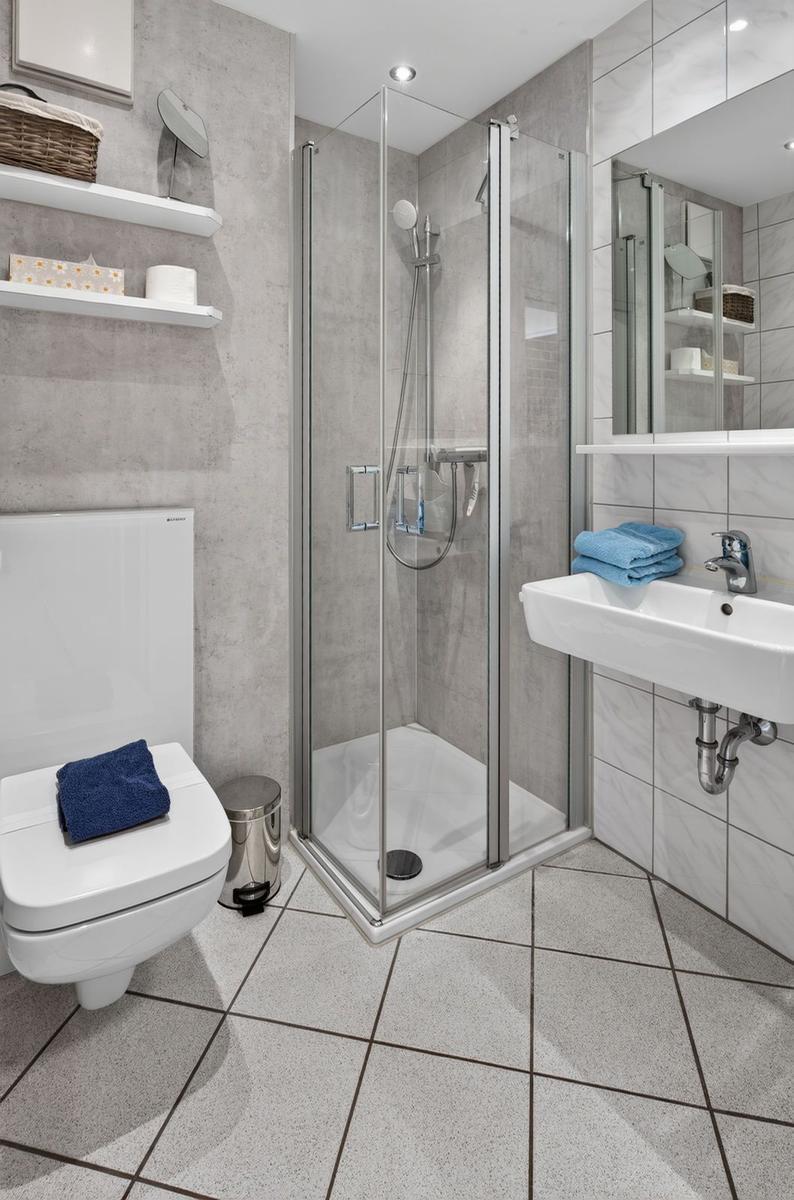 Badezimmer mit Dusche, Waschbecken und Toilette. Fliesenboden und Wandverkleidung.