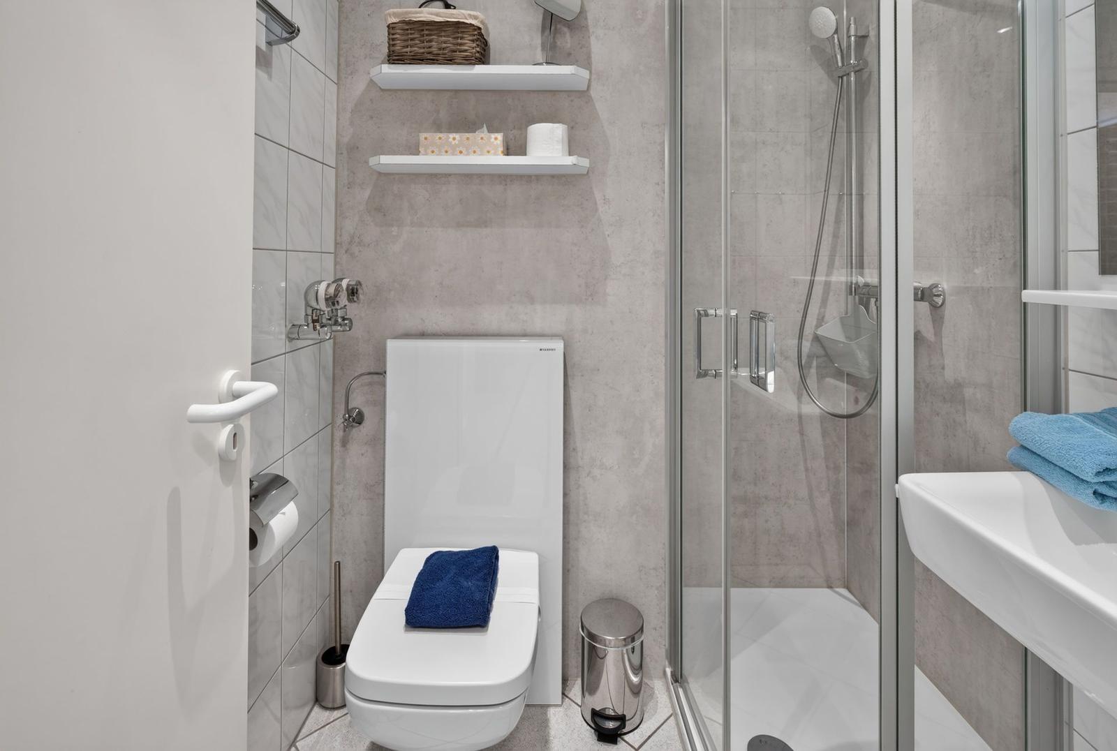Badezimmer mit Dusche, Toilette und Waschbecken. Weiße Fliesen und moderne Einrichtung.