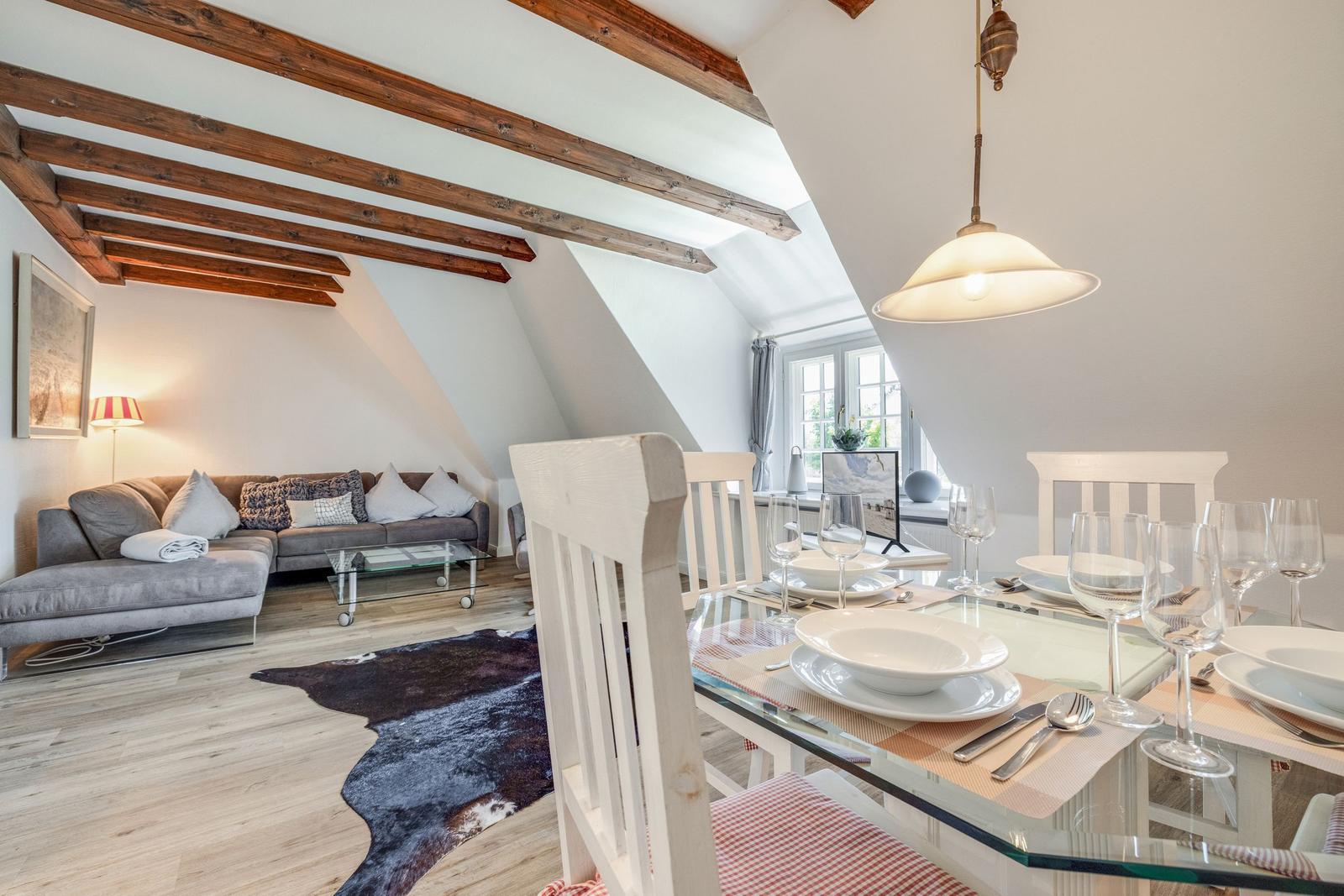 Wohn- und Essbereich mit Holzbalkendecke, Sofa, Esstisch und Fenster.