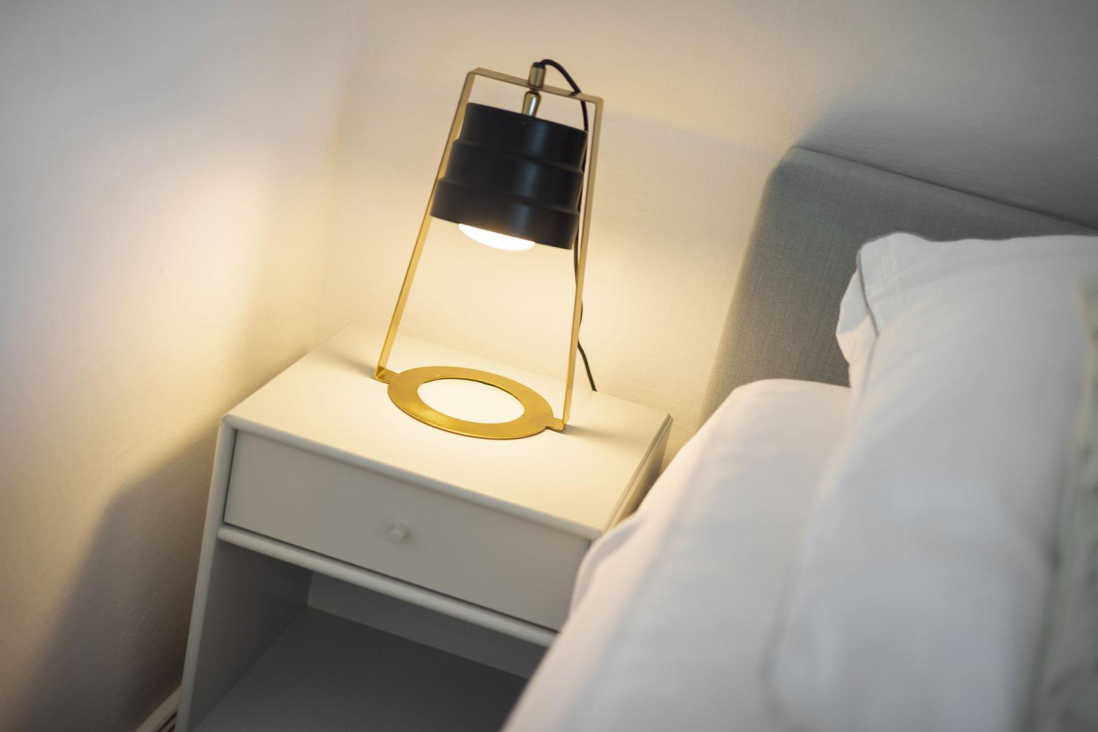 Schlafzimmer mit Nachttisch und Lampe. Bett mit weißer Bettwäsche.