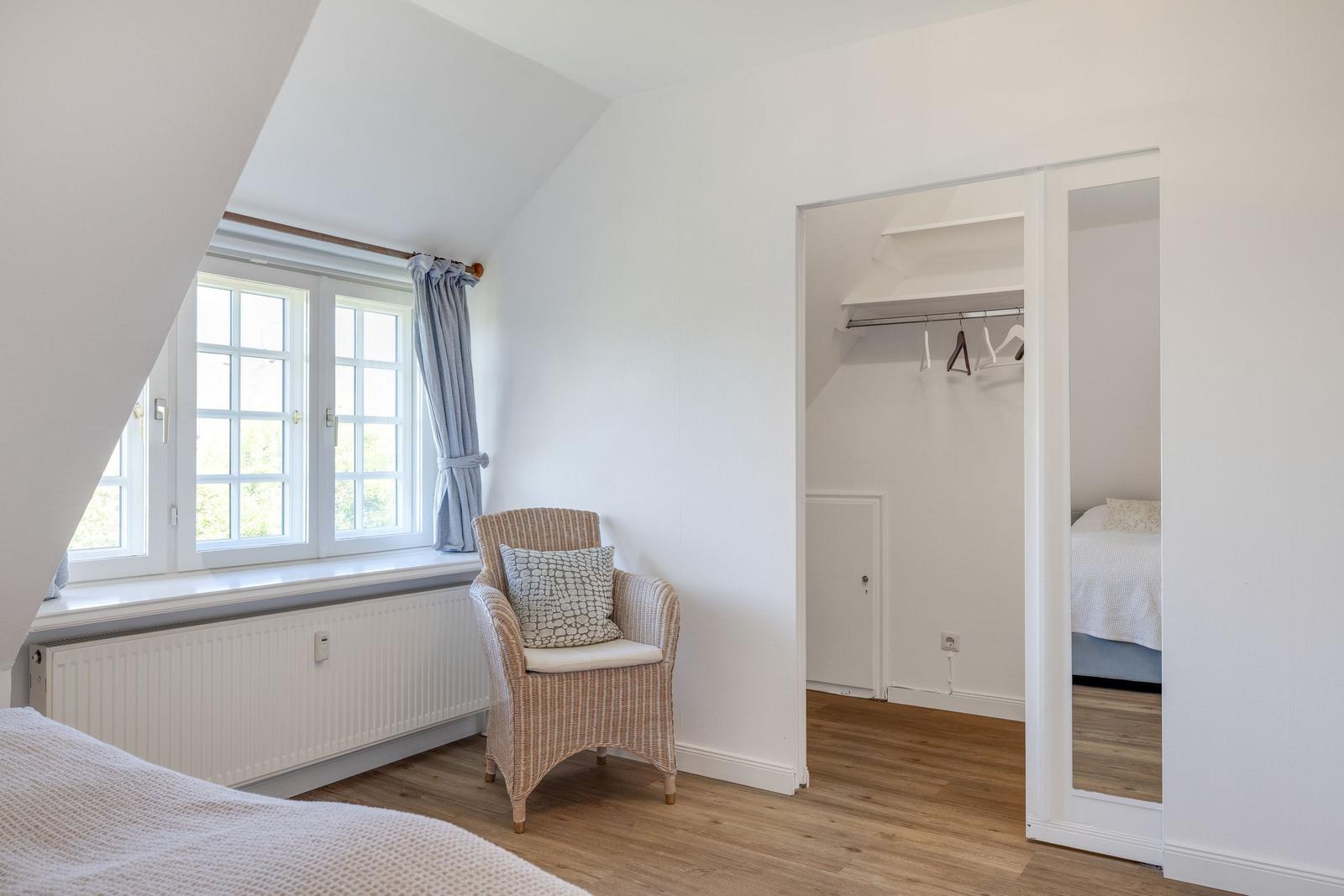 Schlafzimmer mit Dachschräge, Fenster, Stuhl und Blick in die Garderobe.