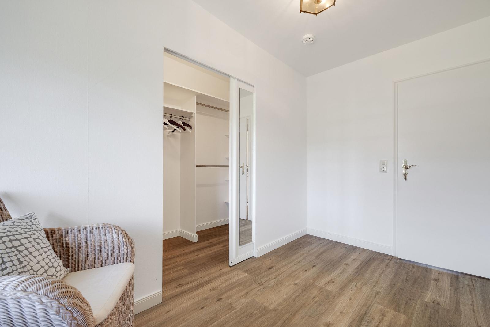 Zimmer mit Kleiderschrank, Holzboden und Wicker-Sofa mit Kissen.