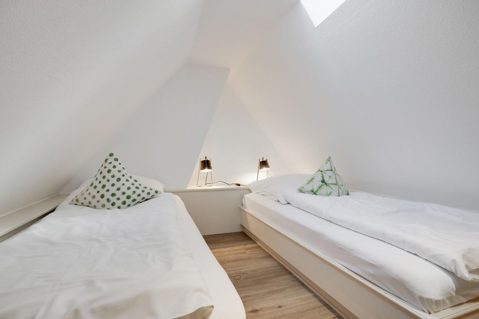 Zwei Einzelbetten in einem Dachzimmer mit weißen Wänden und Holzboden.