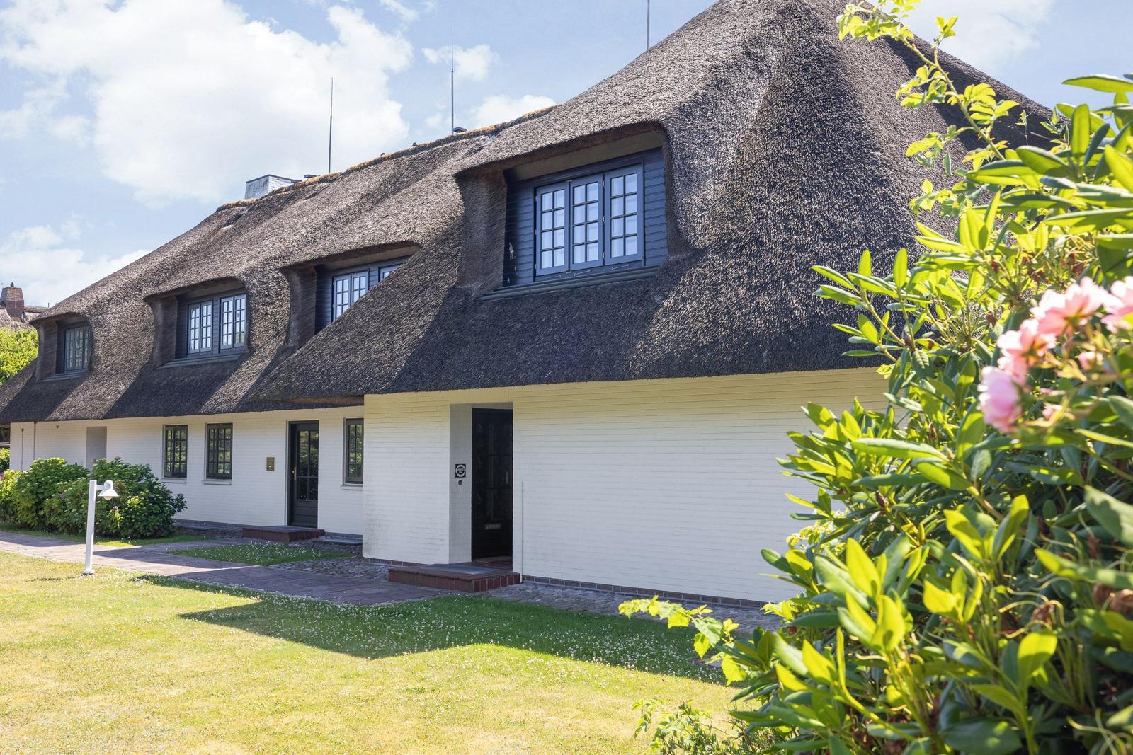 Haus mit strohgedecktem Dach, weißen Wänden und Fenstern mit dunklen Rahmen.