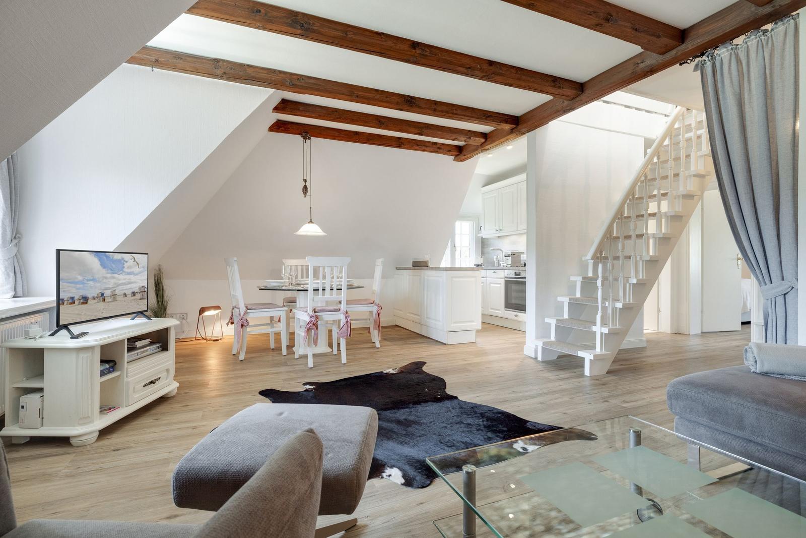 Wohn- und Essbereich mit Holzbalken, Küchenzeile und Treppe.