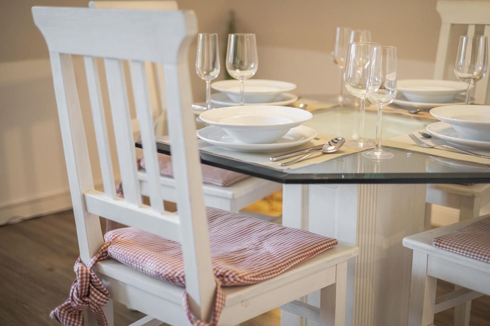Glas-Tisch mit weißen Stühlen und roten Sitzkissen. Geschirr und Gläser sind darauf platziert.