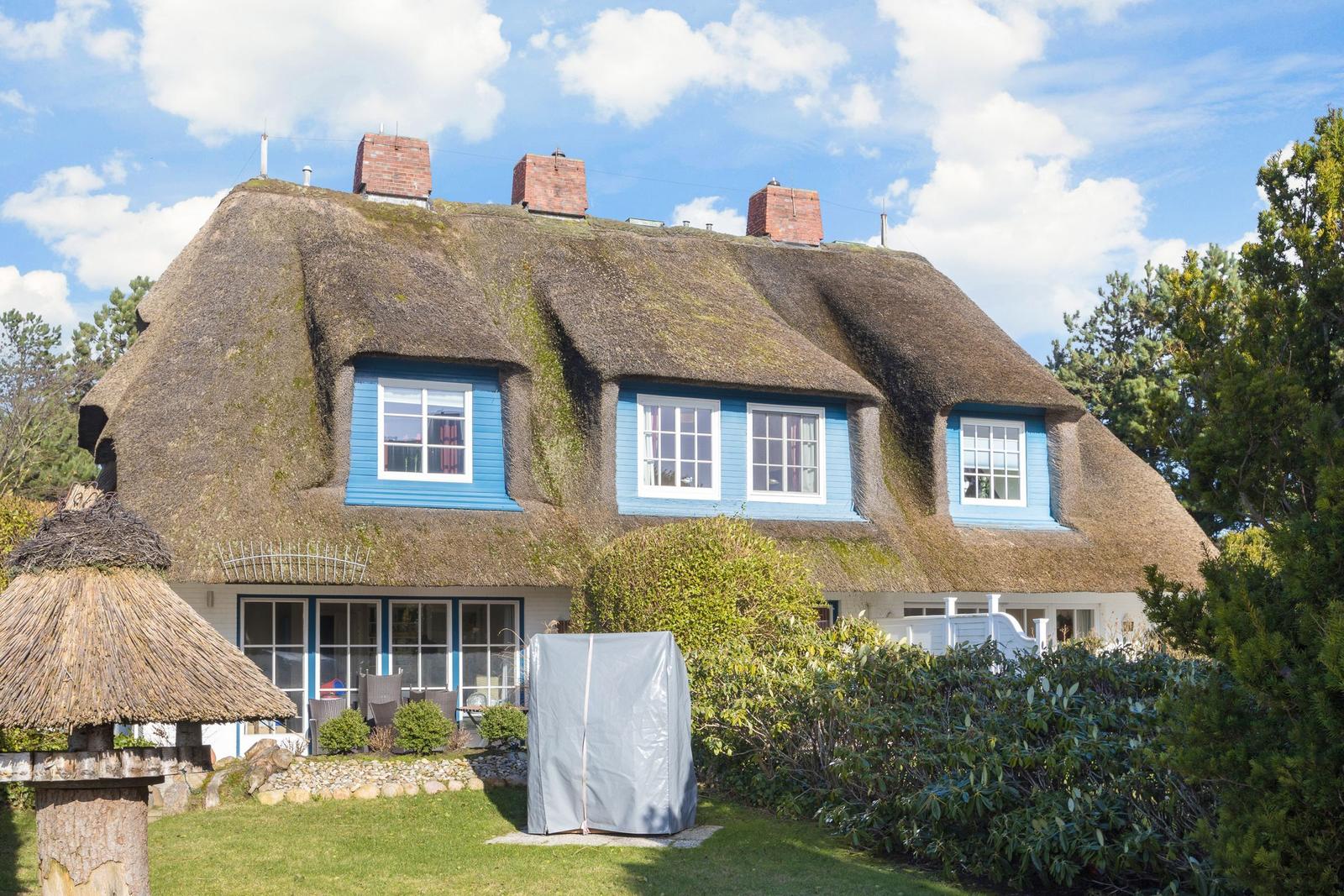 Haus mit strohgedecktem Dach und blauen Fenstern im Garten