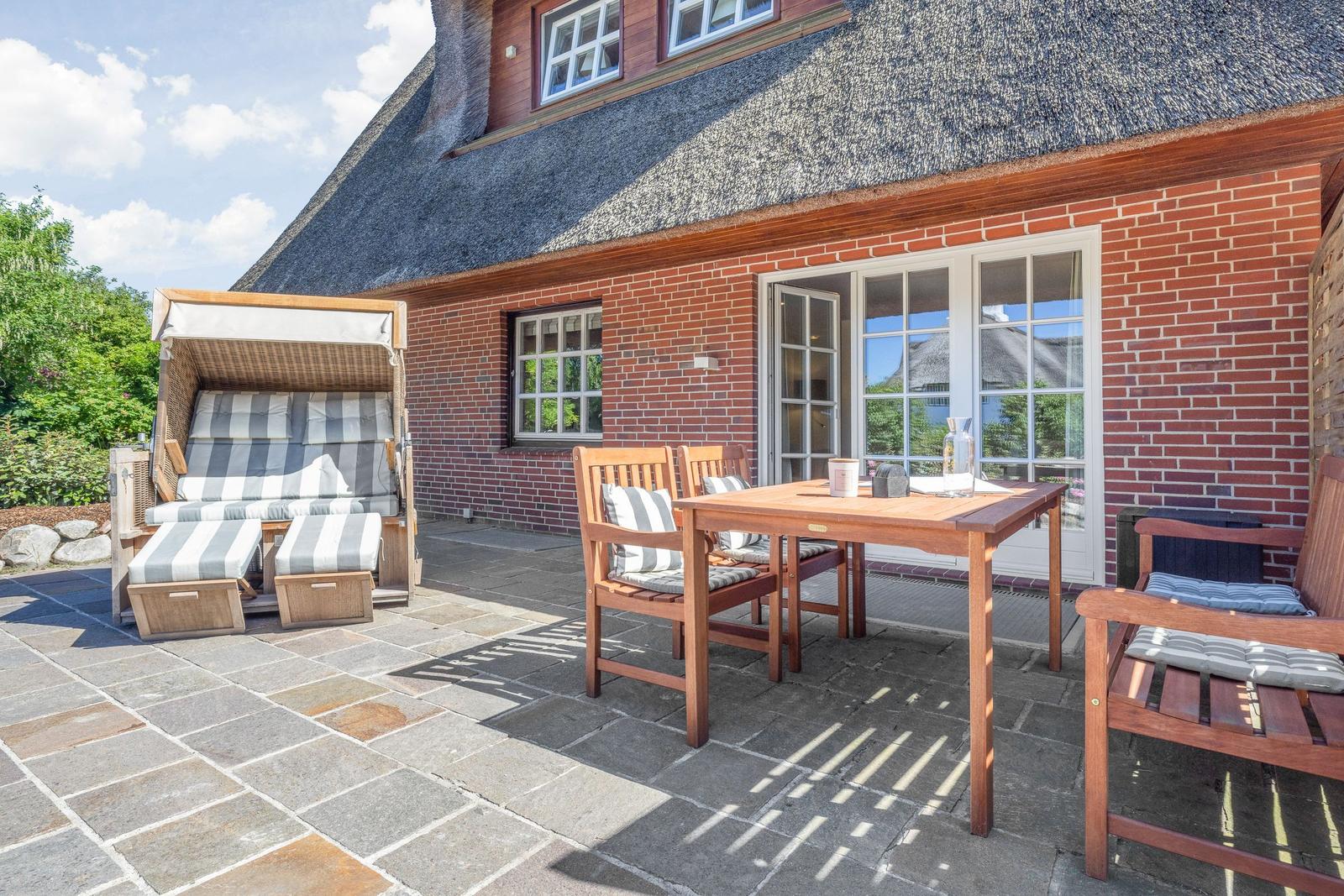 Terrasse mit Holztisch, Stühlen und Strandkorb vor einem Haus mit Schieferdach.