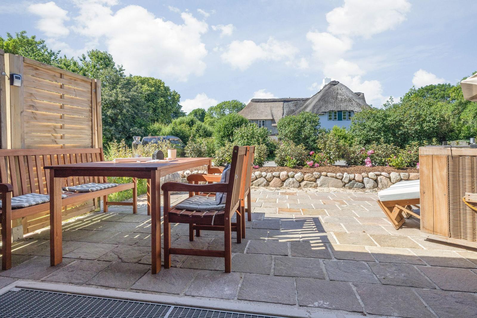 Terrasse mit Holztisch, Stühlen und Blick auf ein Haus mit Strohdach.