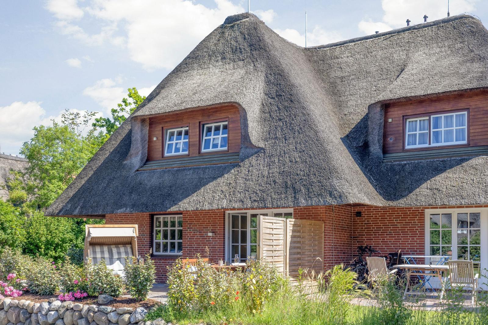 Haus mit Strohdach, Terrasse und Garten. Fenster und Türen sind sichtbar.