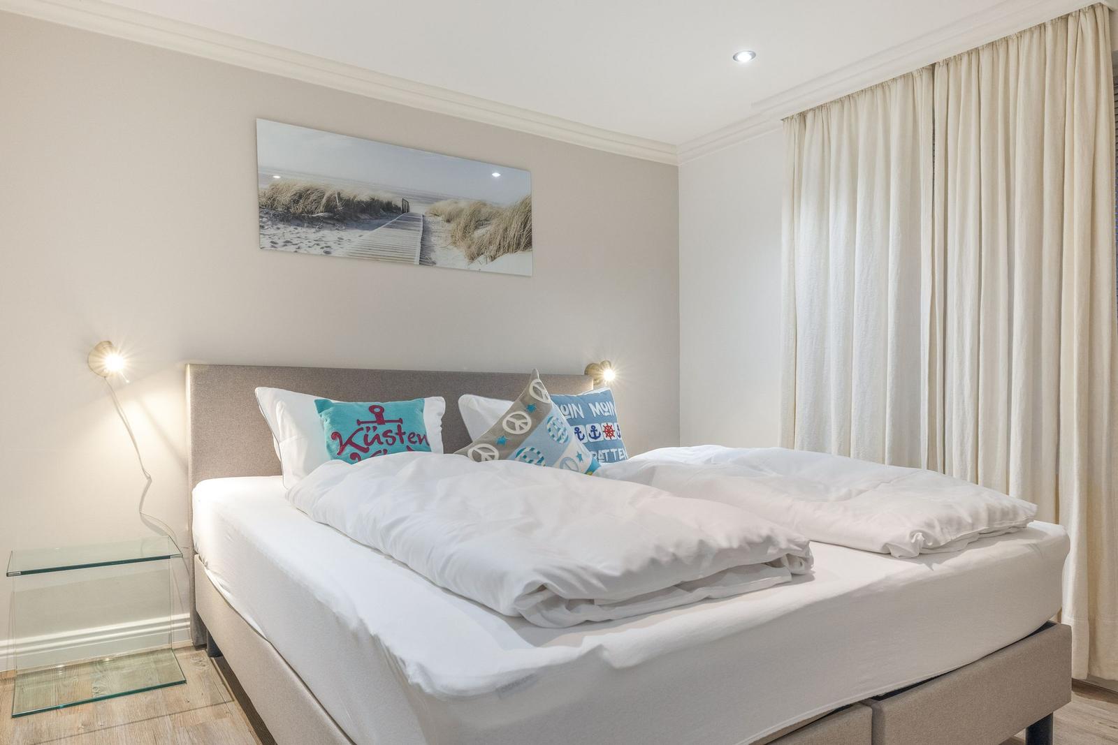 Schlafzimmer mit Doppelbett, Wandbild und cremefarbenen Vorhängen.