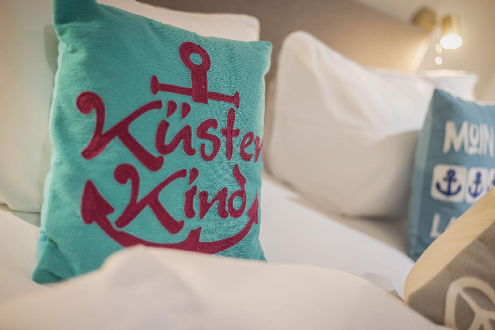Bettkopfteil mit Kissen, eines mit Aufschrift Küstenkind und Anker