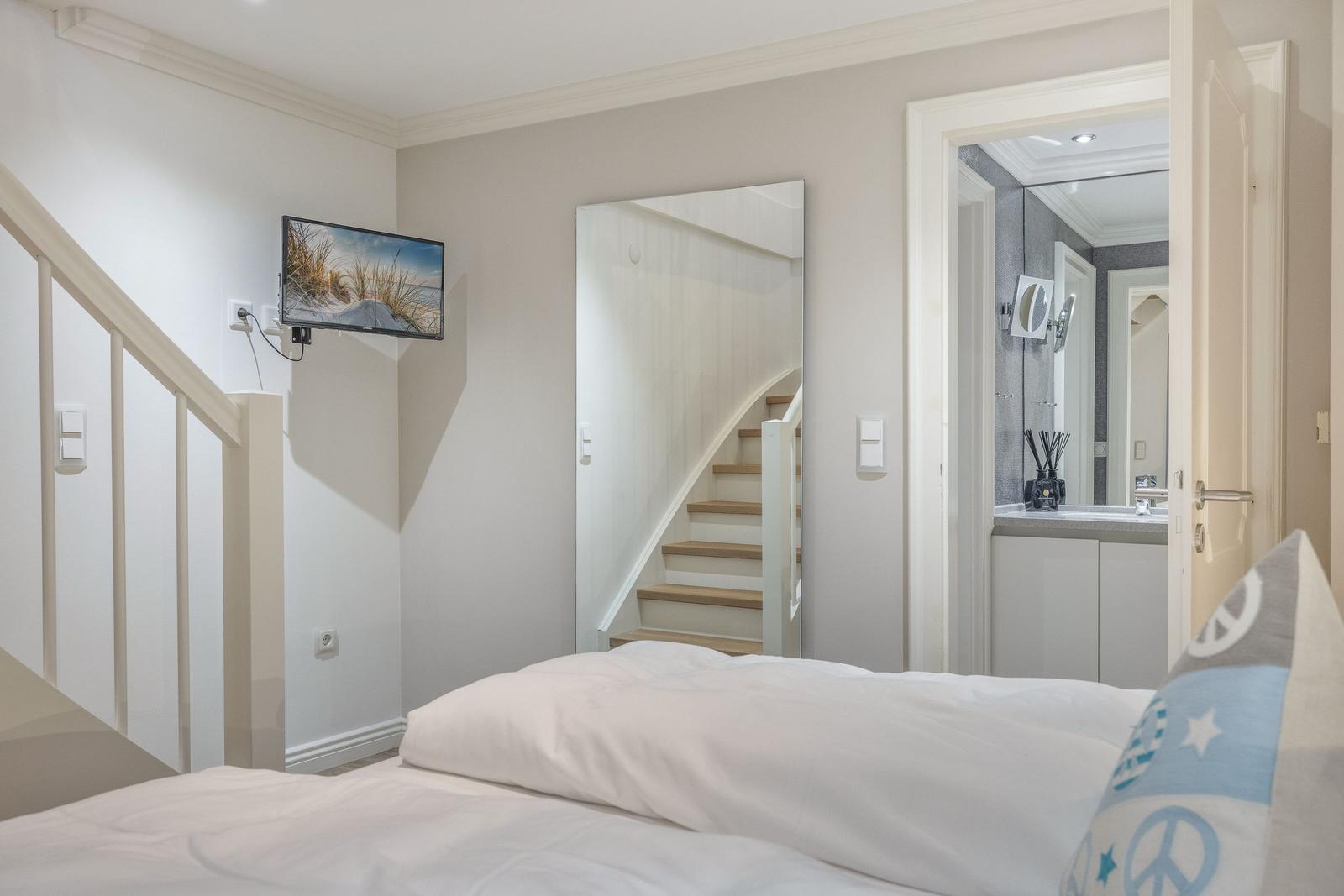Schlafzimmer mit Bett, TV und Blick auf die Treppe und das Badezimmer.