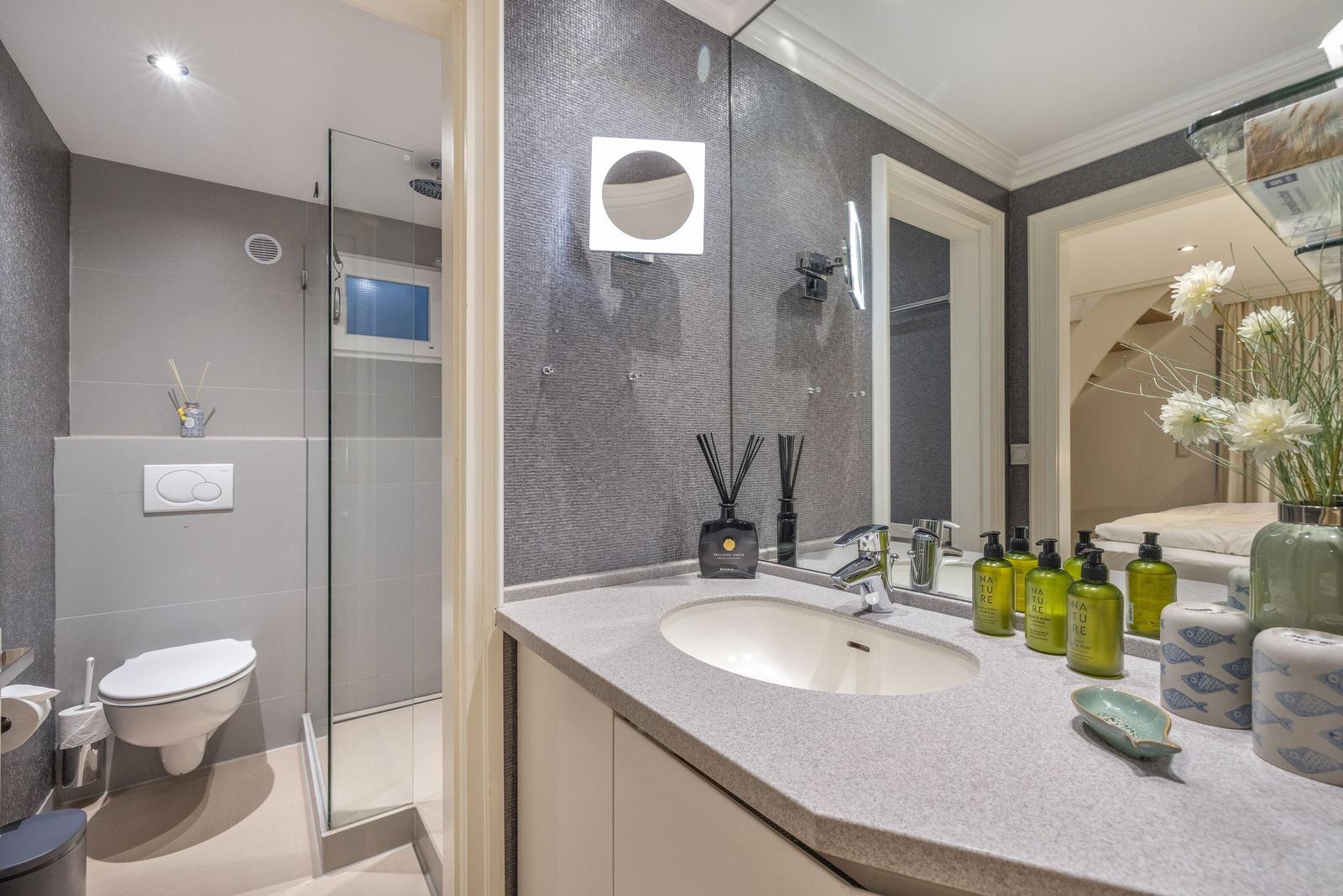 Bad mit Waschbecken, Spiegel und Dusche mit Glaswand.