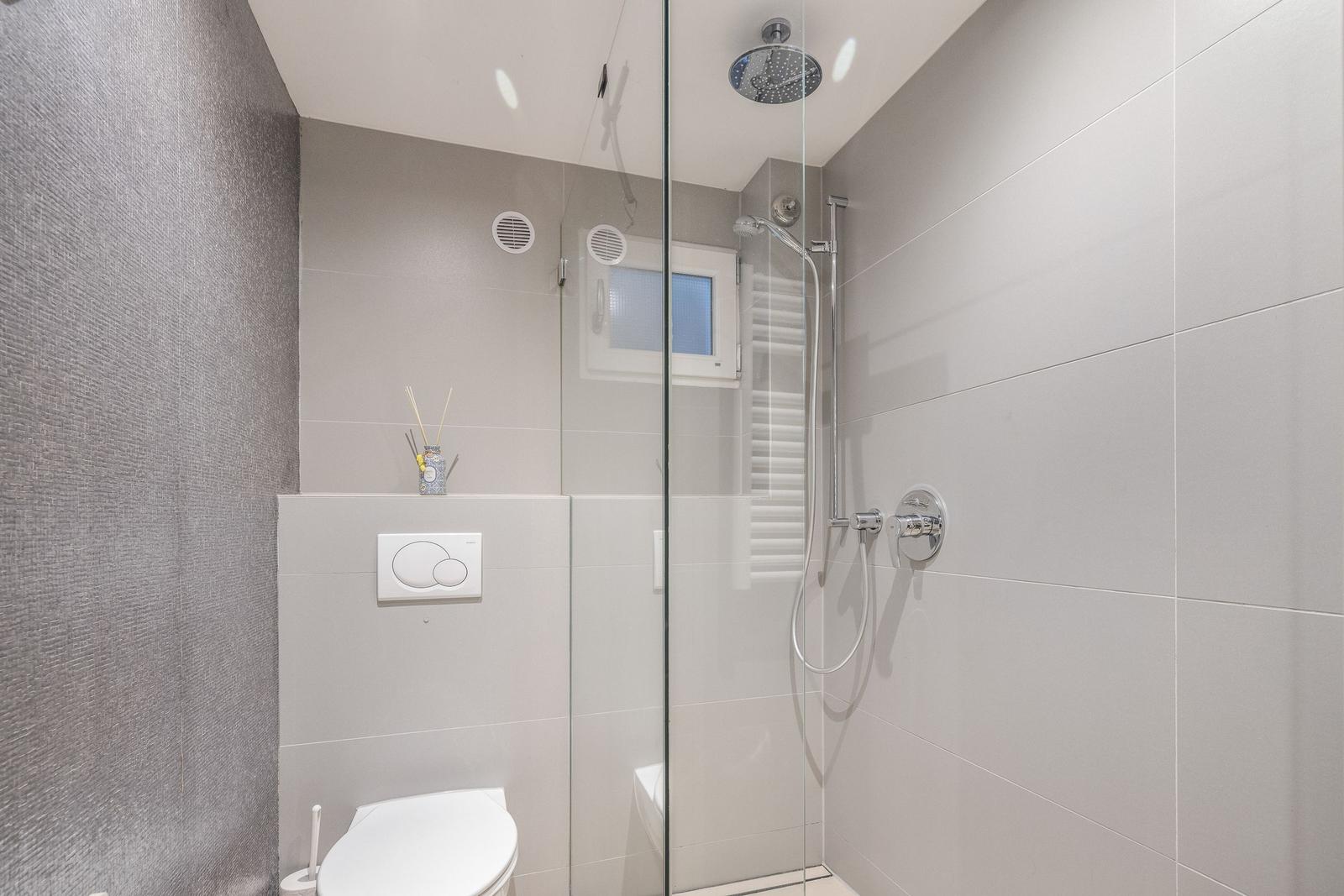 Bad mit Dusche, Toilette und Fenster. Glaswand trennt Dusche.