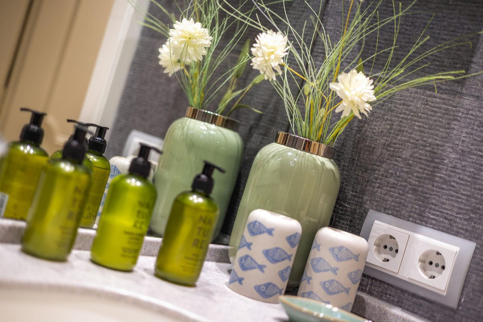 Badezimmer mit grünen Flaschen, Vasen und Blumen auf der Arbeitsplatte.
