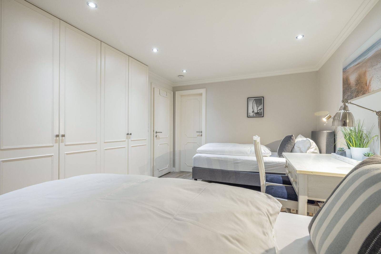 Zwei Betten, Schrank, Tisch und Wandbild in einem Schlafzimmer.