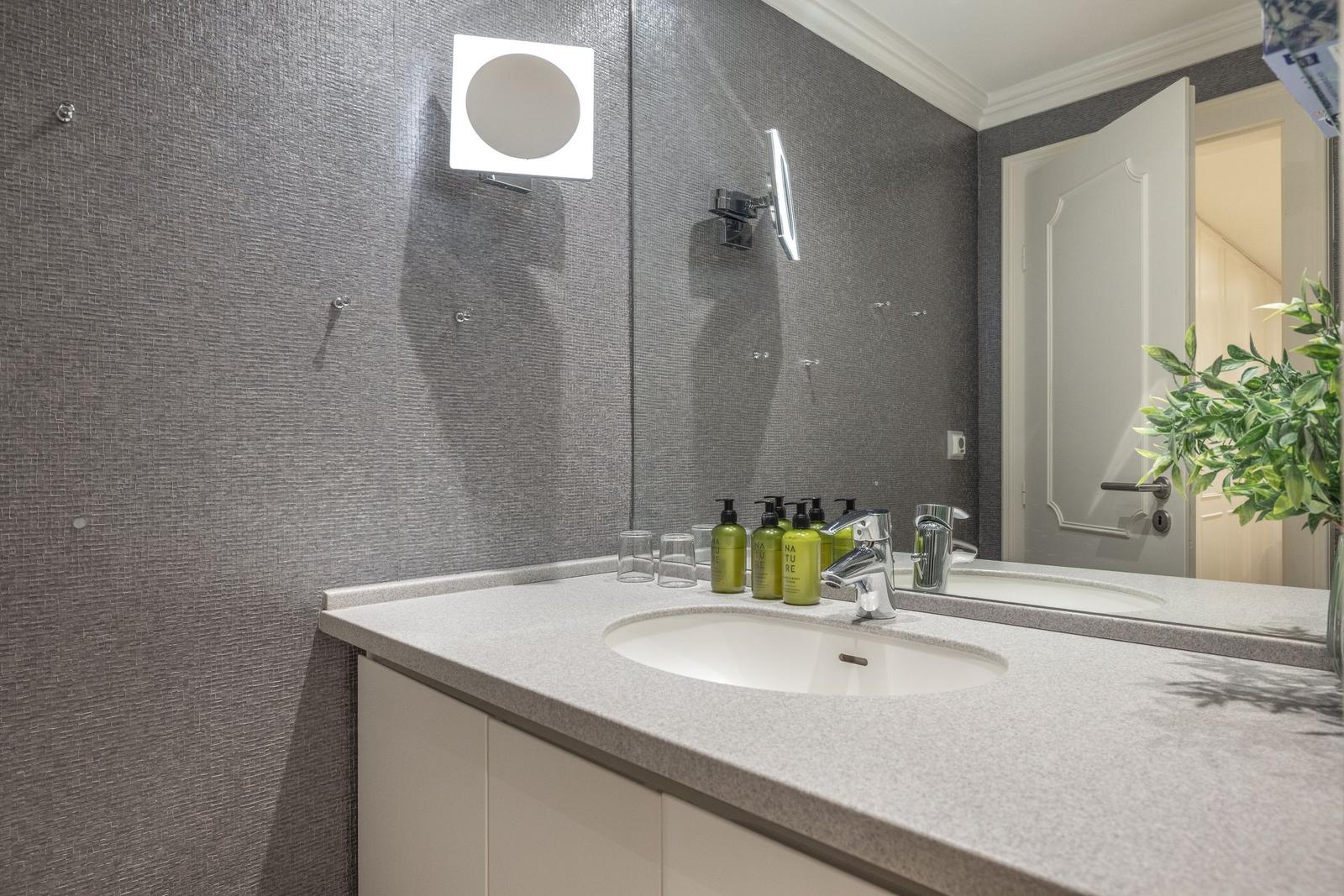 Badezimmer mit Waschbecken, Spiegel und grünen Flaschen.
