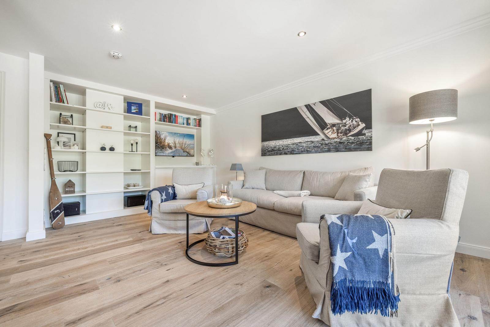 Wohnzimmer mit Sofa, Sessel, Couchtisch und Bücherregal an der Wand.