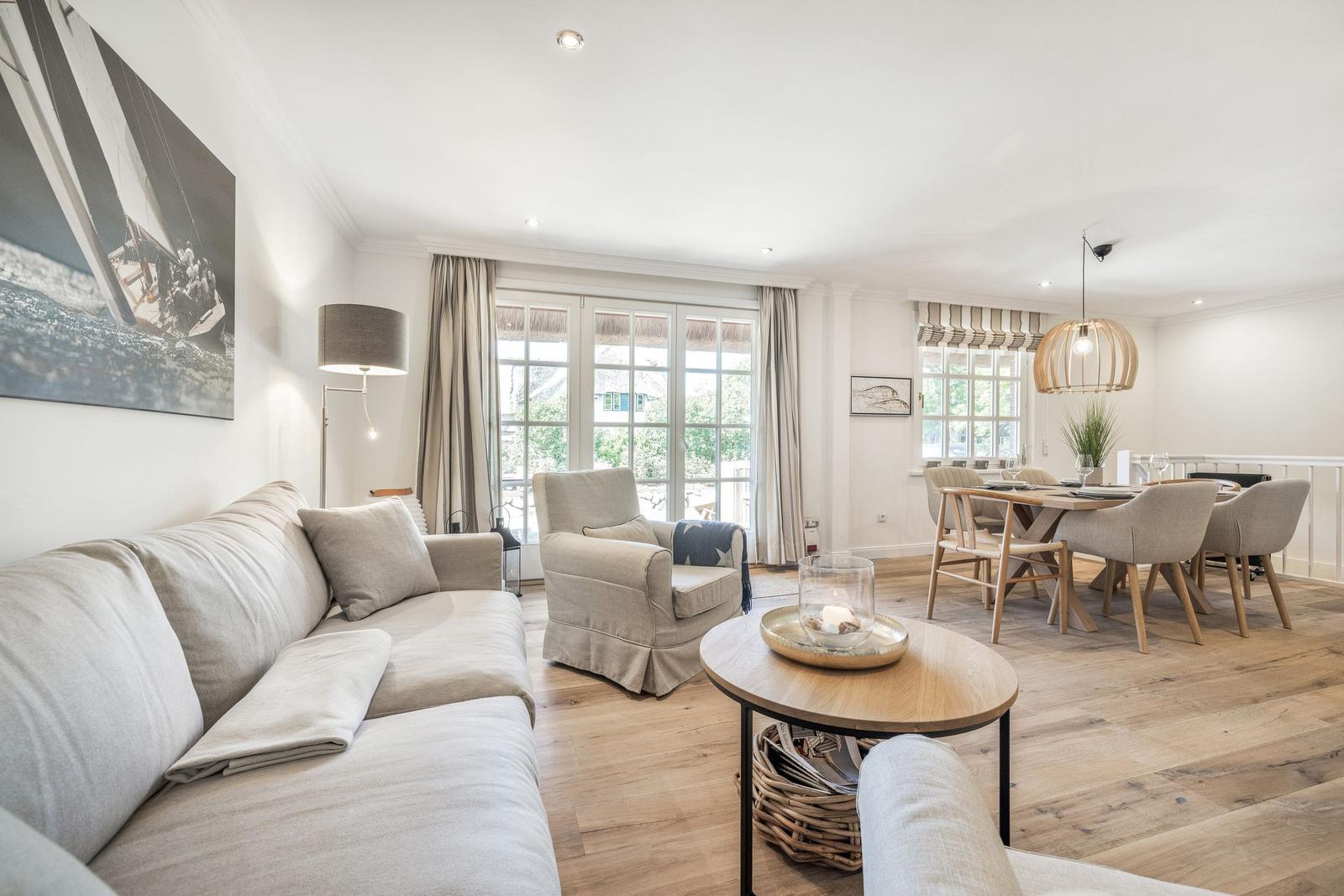 Wohn- und Essbereich mit Sofa, Sessel, Tisch und Stühlen. Holzboden und große Fenster.