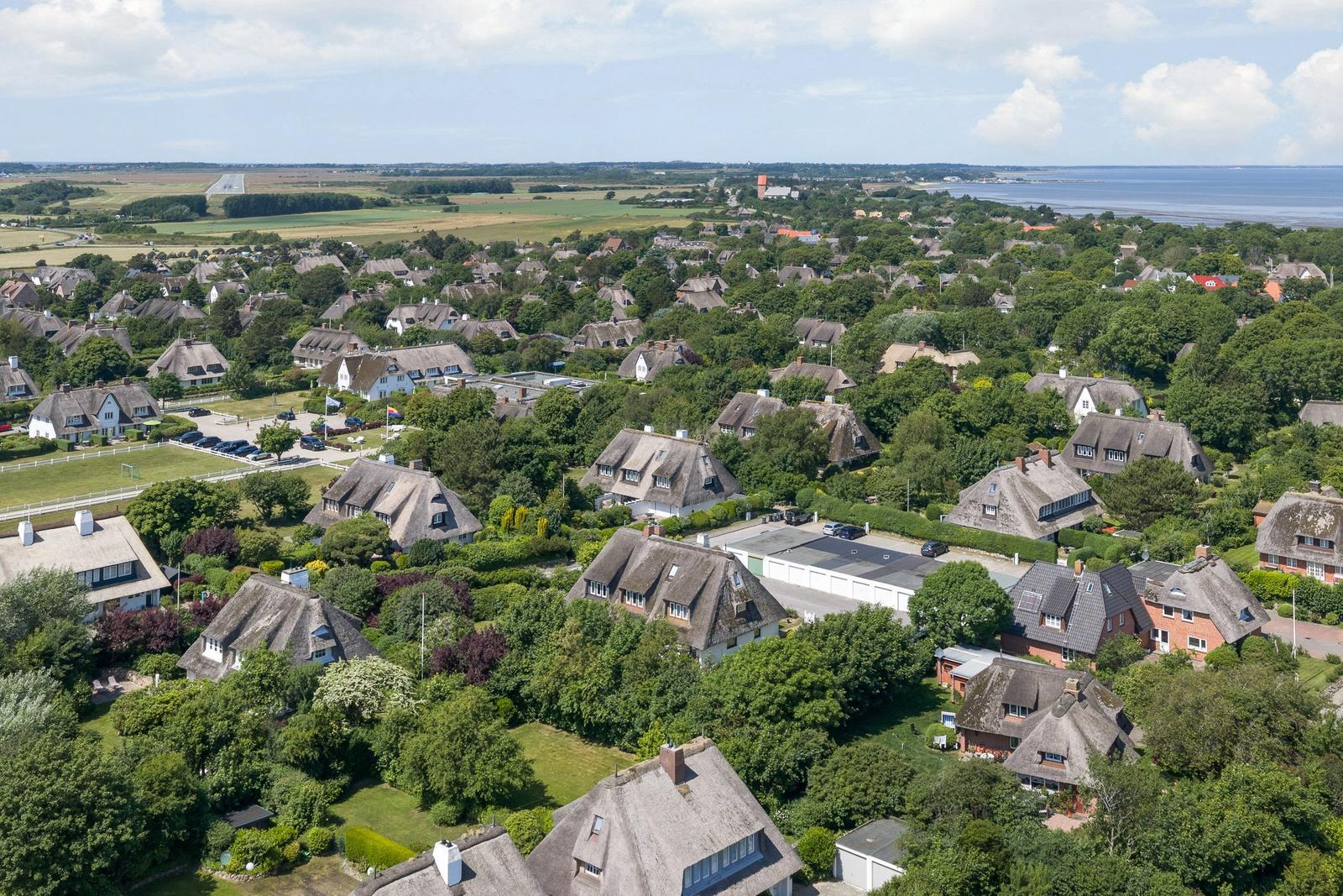 Dorf mit strohgedeckten Häusern, grünen Gärten und Blick auf Meer und Flugfeld.