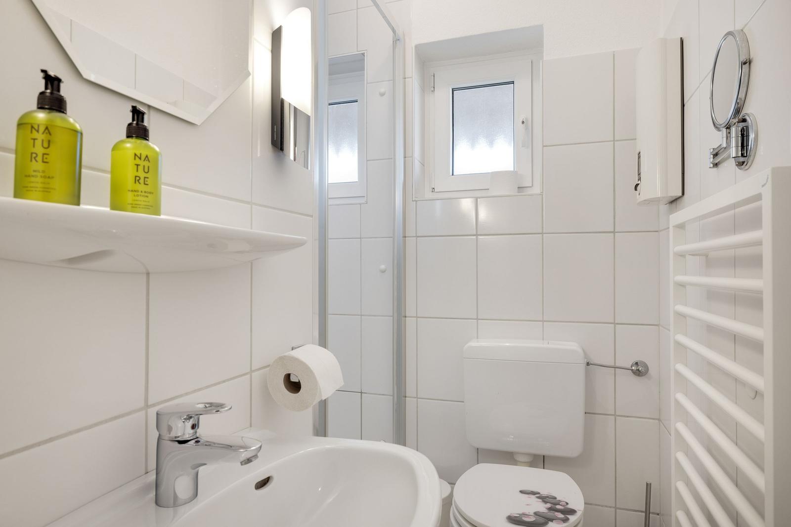 Badezimmer mit Dusche, Toilette, Waschbecken und Spiegel.