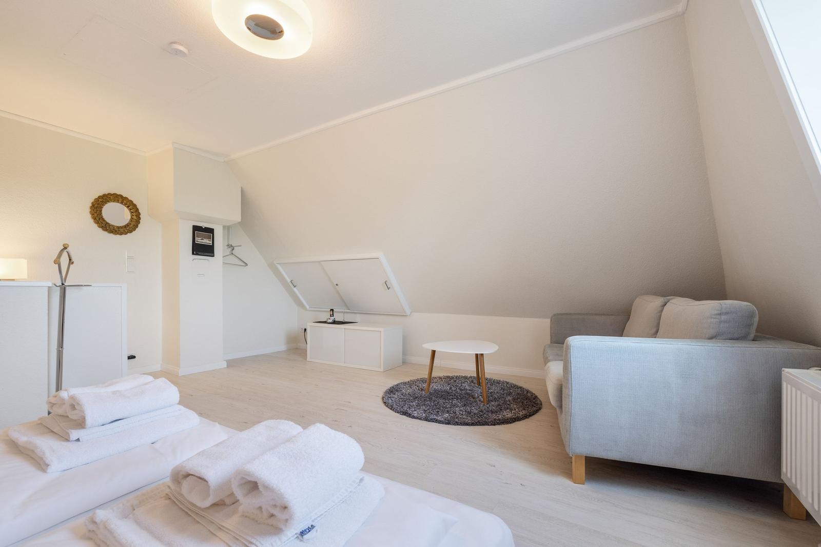 Schlafzimmer mit Bett, Sofa und Kleiderschrank unter Dachschräge.