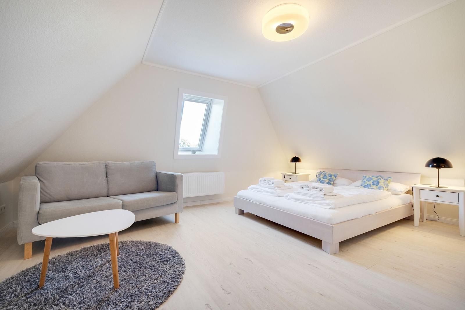 Ein Schlafzimmer mit Dachschrägen, Bett, Sofa und Tisch.