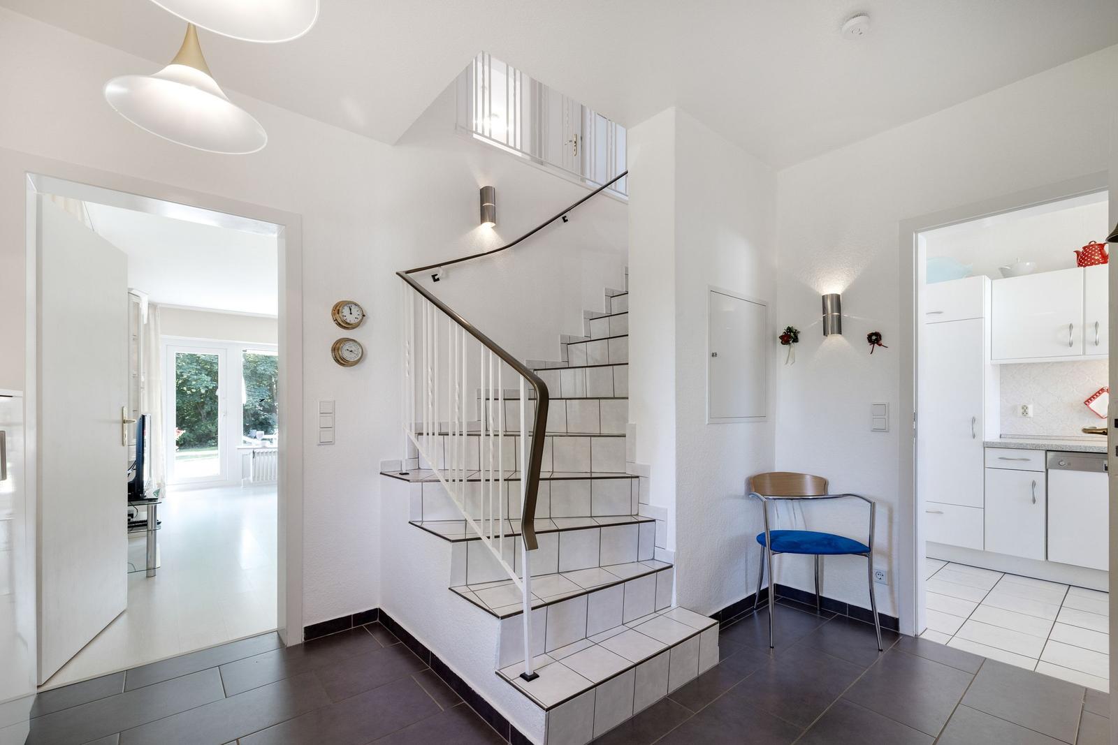 Haus mit Treppe, Küche und Wohnzimmer. Ein blauer Stuhl und Wanduhren sind sichtbar.