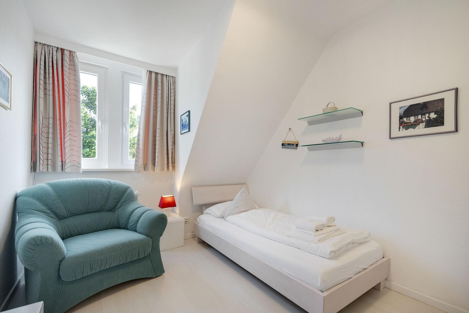 Ein Schlafzimmer mit einem Bett, einem Sessel und einem Fenster mit Vorhängen.