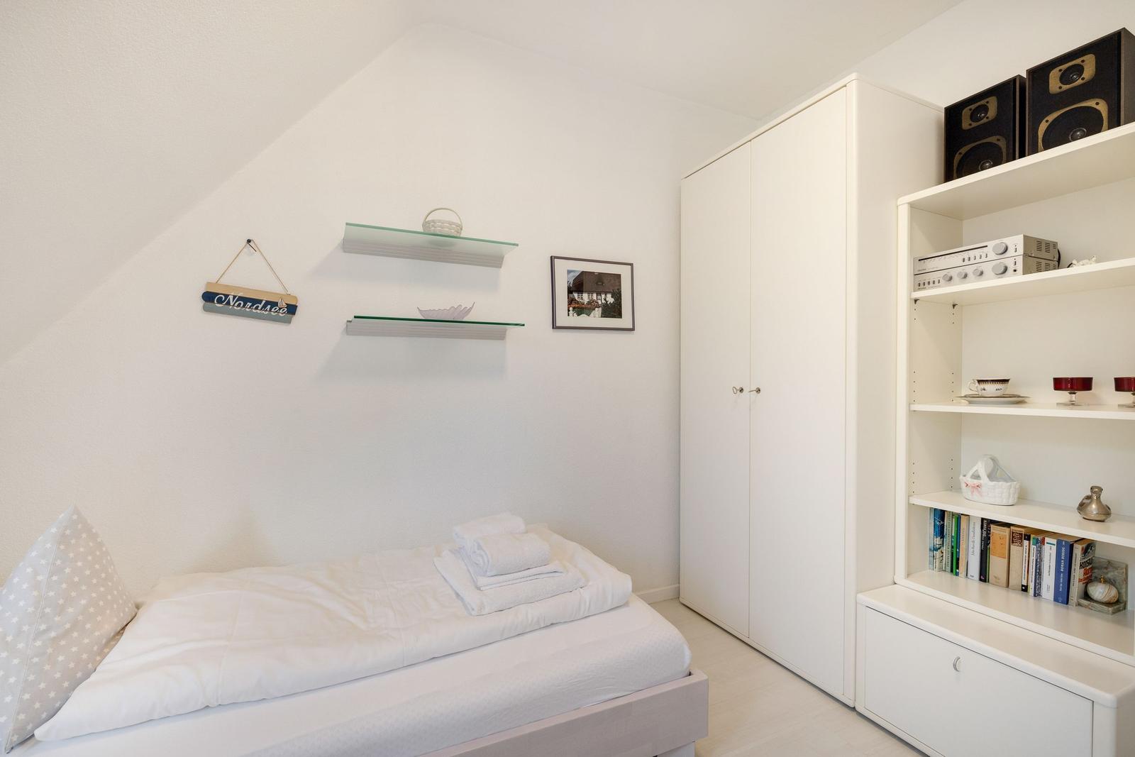 Schlafzimmer mit Bett, Kleiderschrank und Regal mit Büchern und Audioequipment.