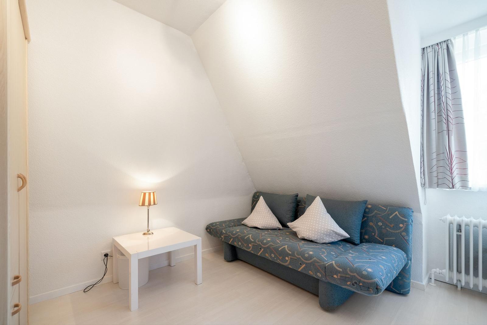 Zimmer mit Sofa, Tisch und Lampe unter schrägen Wänden
